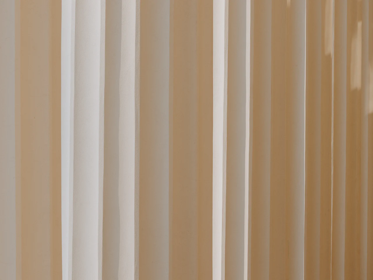Beige and white striped drapery lit to show its vertical fall