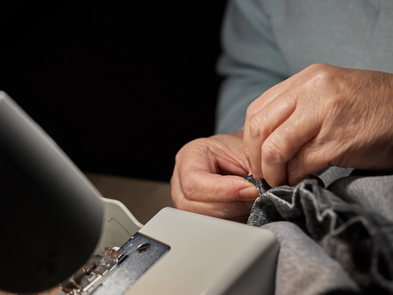 Hands guiding grey fabric through a sewing machine