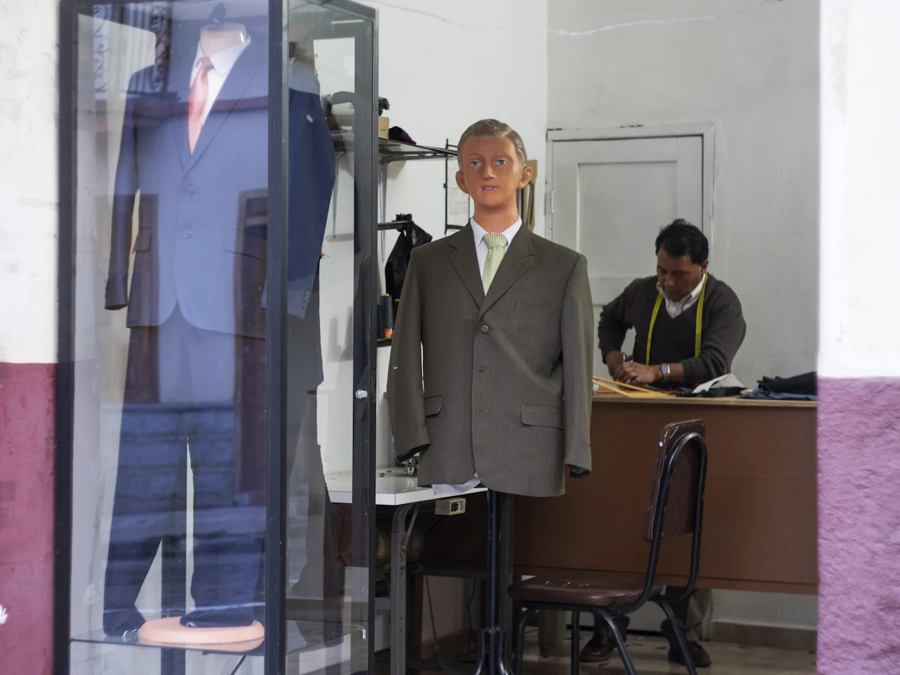 A tailor at work behind a mannequin in a shop window